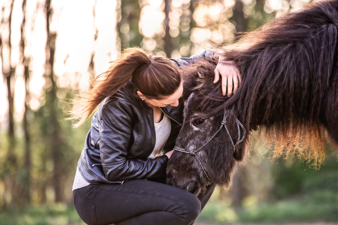 achtsames-pferdetraining-tabea-richter-2 dunkelhaarige Frau umarmt schwarzes Shetlandpony mit Knotenhalfter