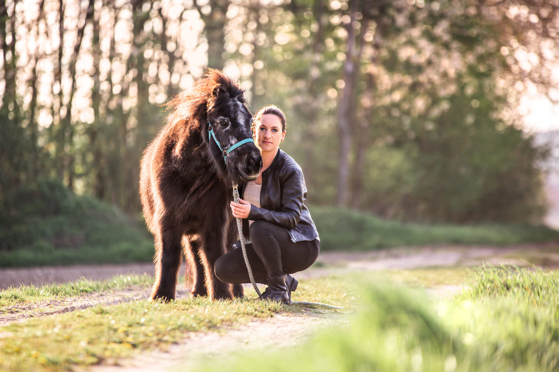 achtsames-pferdetraining-tabea-richter schwarzes Shetlandpony mit kniender Frau in Natur
